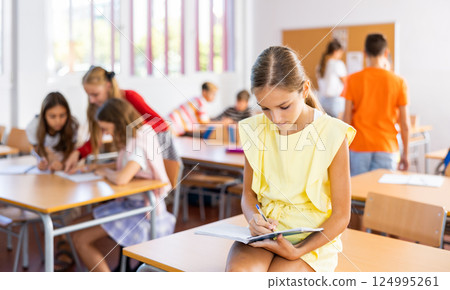 Portrait of schoolgirl with notebook in her hands who sits on desk in school class Portrait of schoolgirl with notebook in her hands who sits on desk in school class 124995261
