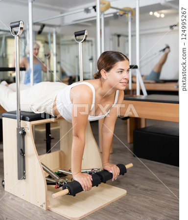 Young girl practicing pilates stretching exercises on combo chair Young girl practicing pilates stretching exercises on combo chair 124995267