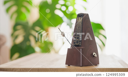 Vintage metronome ticking on wooden table with green foliage background 124995309