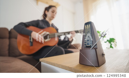 Musician practicing guitar using traditional metronome at home 124995348