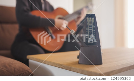 Musician practicing guitar using a metronome for perfect timing Musician practicing guitar using a metronome for perfect timing 124995363