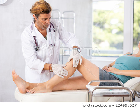 Doctor in medical gloves exam woman's legs. 124995527