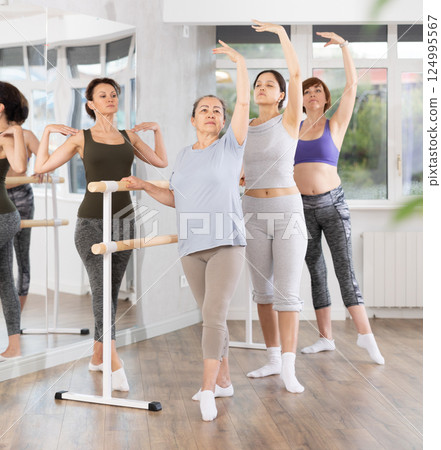 Female ballet enthusiasts mastering basic positions with teacher Female ballet enthusiasts mastering basic positions with teacher 124995567