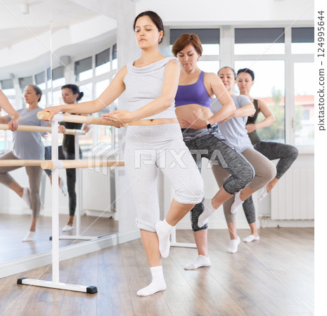 Group of female beginners performing fondue at barre 124995644