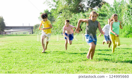 Cheerful preteen boys and girls running on green lawn 124995660