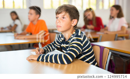 Focused preteen schoolboy writing in workbook during lesson 124995714