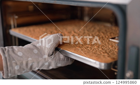 Pastry chef takes out baking sheet with finished cake layer from oven. Dessert 124995860