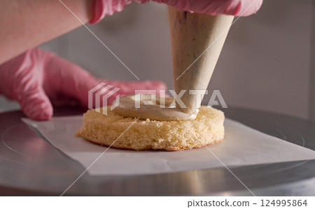 Professional confectioner greasing baked sponge cake with cream. Small bento. 124995864