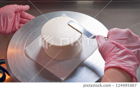 Professional female hands levels cream on baked sponge cake. Dessert decoration. Professional female hands levels cream on baked sponge cake. Dessert decoration. 124995867