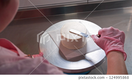 Professional female hands levels cream on baked sponge cake. Dessert decoration. 124995868