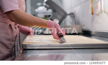 Pastry chef smooths surface of batter on baking parchment. Cooking sponge cake Pastry chef smooths surface of batter on baking parchment. Cooking sponge cake 124995877