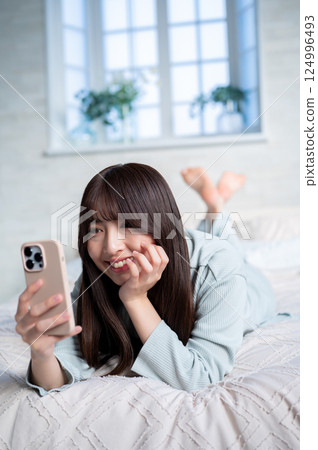 一名女子趴在地上看著自己的智慧型手機 一名女子趴在地上看著自己的智慧型手機 124996493