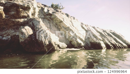 Rocky shoreline with calm water under soft sunlight during evening hours 124996964