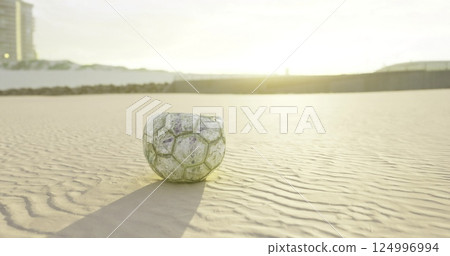Old weathered soccer ball rests on a sandy beach during sunset Old weathered soccer ball rests on a sandy beach during sunset 124996994