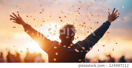 Blurred silhouette of figure throwing confetti at sunset, celebrating joyfully with arms raised. vibrant colors of sky enhance festive atmosphere 124997212