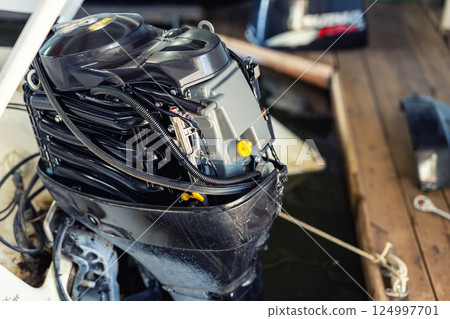 Repairing inflatable motorboat engine at boat garage. Ship engine seasonal service and maintenance. Vessel motor with open cover Repairing inflatable motorboat engine at boat garage. Ship engine seasonal service and maintenance. Vessel motor with open cover 124997701