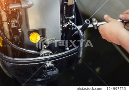 mechanic repairing inflatable motorboat engine at boat garage. Ship engine seasonal service and maintenance. Vessel motor with open cover 124997733