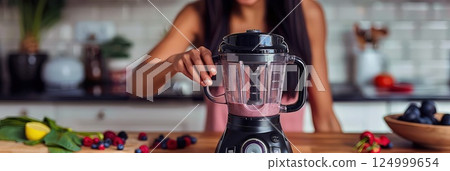 Healthy food concept - Young woman is making a smoothie in the kitchen. The young woman expertly combines fruits and vegetables, crafting a nutrient-packed smoothie for a healthy boost. 124999654