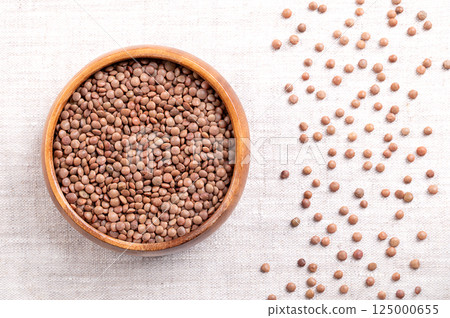 Chateau lentils in a wooden bowl on linen. Dried variety of Lens esculenta, of brownish color, and of delicate and spicey flavor. Also Champagne lentils, because mainly grown in the Champagne region. 125000655