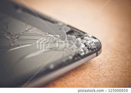 Shattered smartphone screen lying on surface, revealing potential repair costs and device vulnerability from accidental damage 125000850