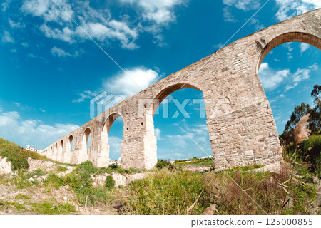 Medieval Kamares aqueduct standing tall against a vibrant blue sky, showcasing remarkable architecture and historical significance Medieval Kamares aqueduct standing tall against a vibrant blue sky, showcasing remarkable architecture and historical significance 125000855
