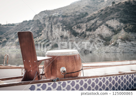 Wooden drum positioned strategically on Dragon Boat, signaling racing rhythm against mountainous lake landscape Wooden drum positioned strategically on Dragon Boat, signaling racing rhythm against mountainous lake landscape 125000865