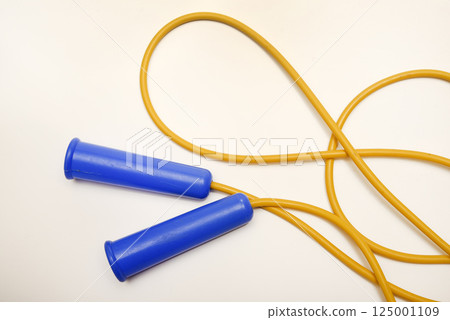A yellow and blue skipping rope on a white background. Sports equipment. A yellow and blue skipping rope on a white background. Sports equipment. 125001109