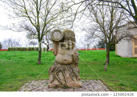 A stone figure of a man with a barrel of wine.A stone figure personifying winemaking. A mustachioed man with a barrel of wine is surrounded by bunches of grapes. 125001426