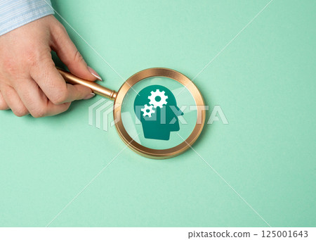 A magnifying glass points to the gears in a person's head. The concept of talent search and thinking development. Analyzing cognitive processes, discovering potential, intellectual growth. 125001643