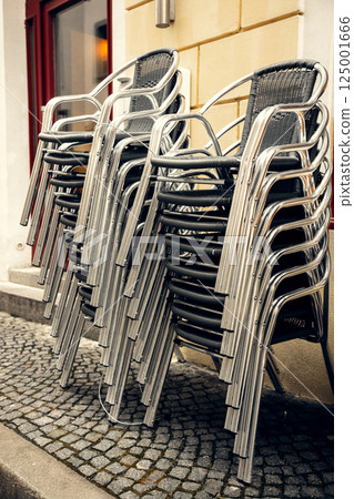 Stacked metal chairs outside European cafe. Neatly stacked metal and wicker chairs outside cafe 125001666