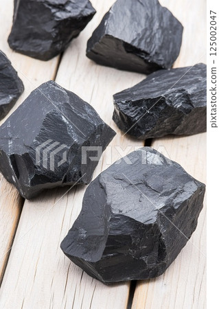 Raw black coal rocks on wooden surface displaying natural texture. 125002047