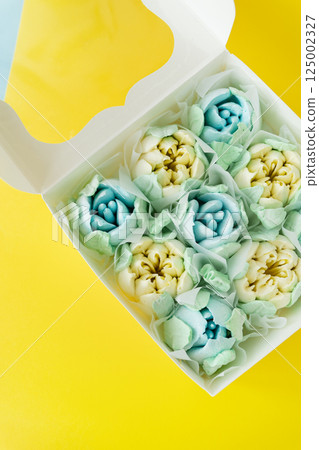 Box of colorful desserts in the shape of flowers on a two-color background. Marshmallow in the form of a rose. 125002327