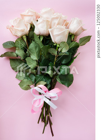 Bouquet of delicate pale pink roses tied with ribbon on a pink background. Romantic floral gift, top view flat lay composition 125002330