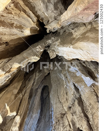 The rocky ceiling of a coastal cave reveals intricate textures and formations above the clear turquoise water, showcasing marine life and geological features below. 125002430