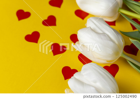 red hearts and white tulip flowers pasted on yellow paper, close up 125002490