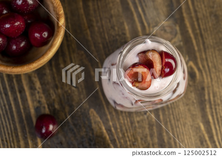 cow cream yogurt with cherry flavor and berry slices, glass jar with cherry yogurt with fresh red cherries closeup, view from above cow cream yogurt with cherry flavor and berry slices, glass jar with cherry yogurt with fresh red cherries closeup, view from above 125002512