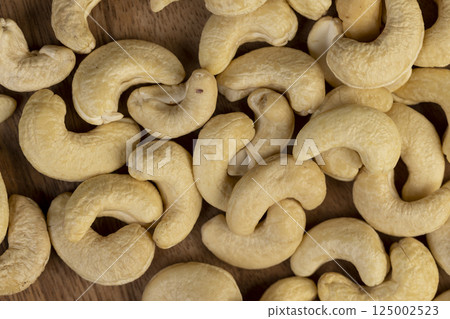 cashew nuts are scattered on a larch board, unroasted cashew nuts are healthy and allowed for vegans. cashew nuts are scattered on a larch board, unroasted cashew nuts are healthy and allowed for vegans. 125002523