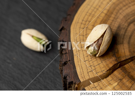 pistachio nuts in their shells with added salt, fried unpeeled pistachio nuts with cracked shells, top view of the object pistachio nuts in their shells with added salt, fried unpeeled pistachio nuts with cracked shells, top view of the object 125002585