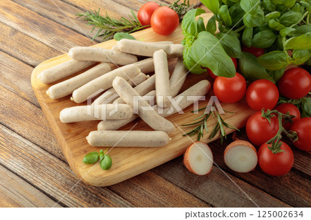 Bavarian white sausages with basil and tomatoes on a cutting board. 125002634