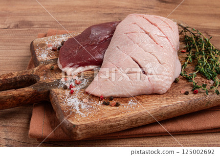 Fresh raw duck breasts, on a wooden chopping board, with herbs and spices, no people 125002692