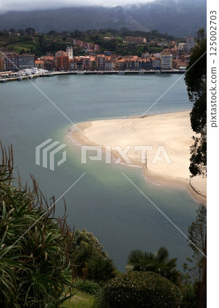 Scenic view of Ribadesella town and sandy beach with cloudy mountain backdrop, Asturias, Spain 125002703