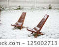 Wooden deck chairs covered with fresh snow in backyard garden after unexpected spring snowfall 125002713