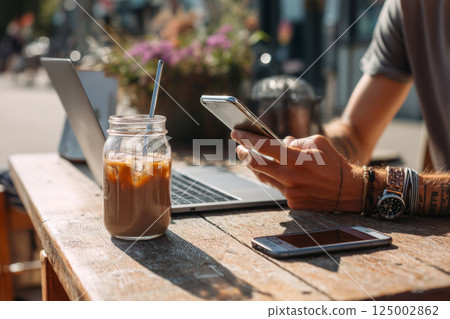 Hands holding phone at street cafe with drink and laptop 125002862
