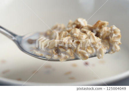 Spoon holding creamy oatmeal with milk and grains in close-up 125004049