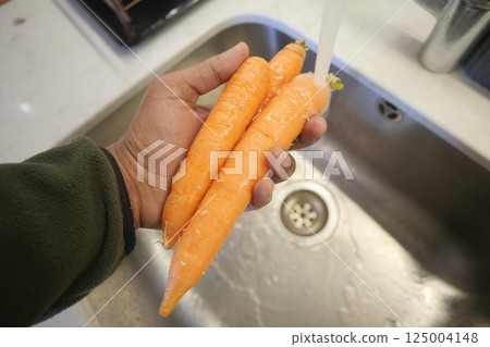 Freshly washed carrots in hand over a kitchen sink during meal prep 125004148