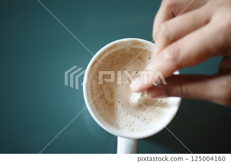 Stirring hot beverage in a white mug on a green table Stirring hot beverage in a white mug on a green table 125004160