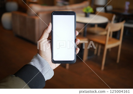Empty smartphone held in hand inside a cozy cafe setting Empty smartphone held in hand inside a cozy cafe setting 125004161