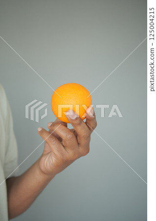 Holding a bright orange fruit in hand against a plain background 125004215