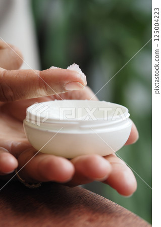 Hand applying petroleum jelly from white container in indoor setting Hand applying petroleum jelly from white container in indoor setting 125004223