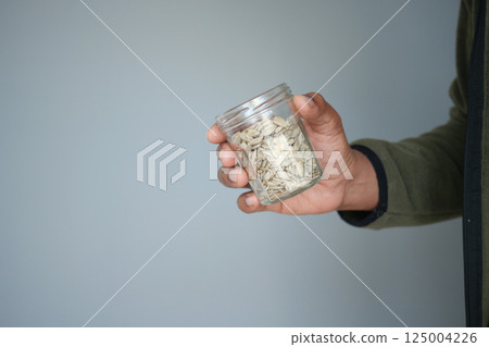 Hand holding a jar filled with seeds against a light background 125004226